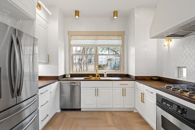 kitchen with light parquet floors, appliances with stainless steel finishes, white cabinetry, and sink