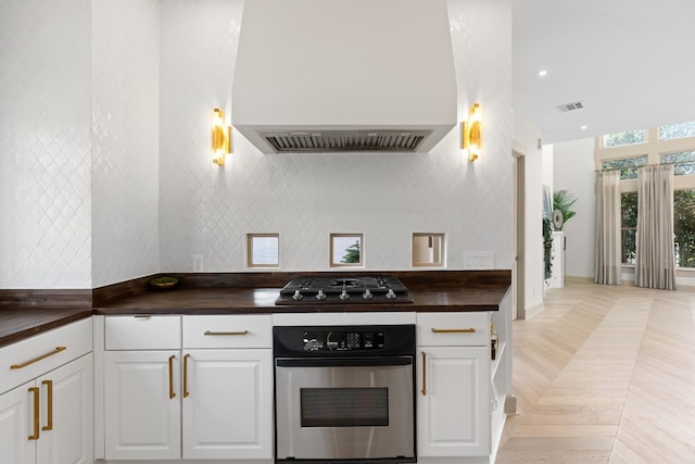 kitchen featuring gas cooktop, premium range hood, stainless steel oven, light parquet floors, and white cabinets