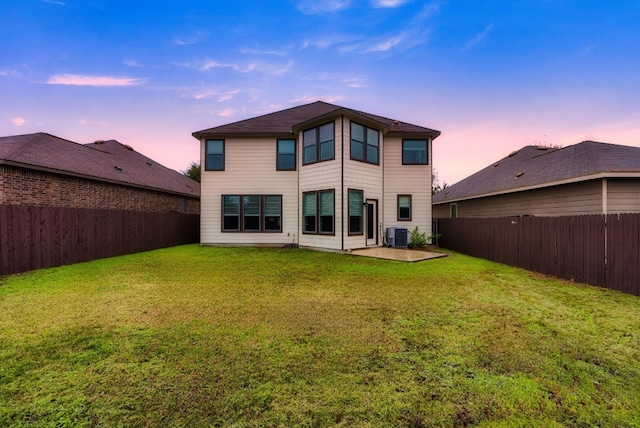 back house at dusk with a lawn, cooling unit, and a patio