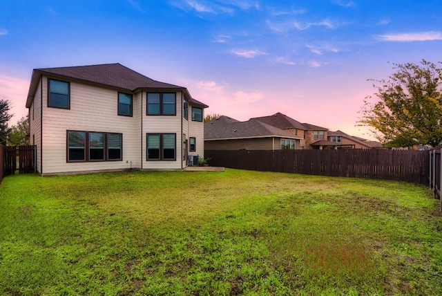 back house at dusk featuring a lawn and central air condition unit