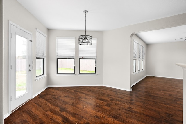 unfurnished dining area with ceiling fan with notable chandelier and dark hardwood / wood-style flooring