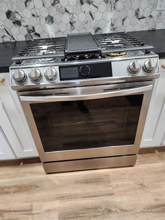 room details with backsplash, white cabinets, light wood-type flooring, and stainless steel gas range