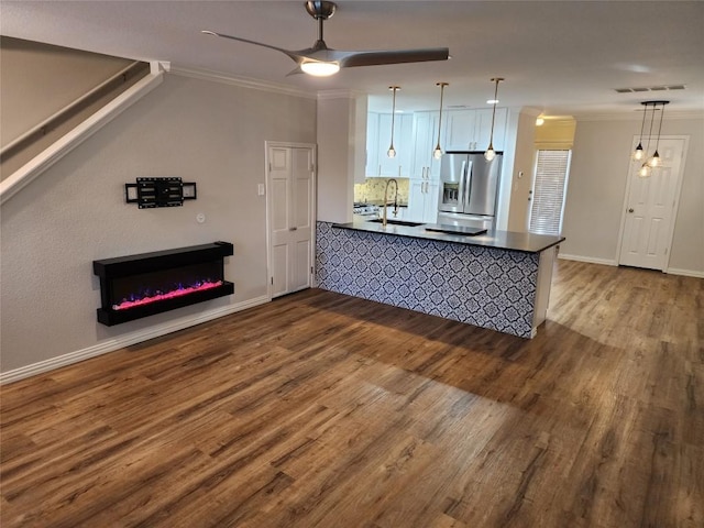 kitchen featuring kitchen peninsula, stainless steel fridge, sink, decorative light fixtures, and white cabinets