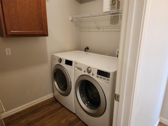 laundry area featuring washing machine and clothes dryer, dark hardwood / wood-style flooring, and cabinets