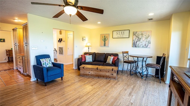 living room with a textured ceiling, light wood-type flooring, and ceiling fan