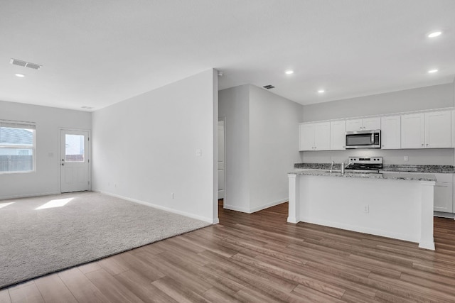 kitchen with white cabinets, a center island with sink, light wood-type flooring, appliances with stainless steel finishes, and light stone counters