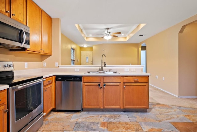 kitchen with a tray ceiling, kitchen peninsula, sink, and appliances with stainless steel finishes