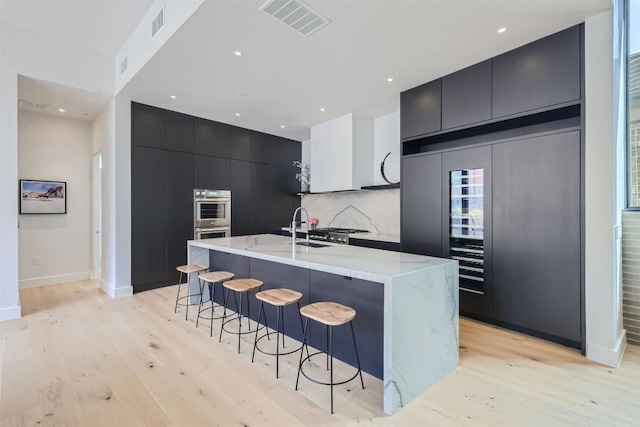 kitchen featuring a breakfast bar, backsplash, light hardwood / wood-style floors, paneled refrigerator, and a center island with sink