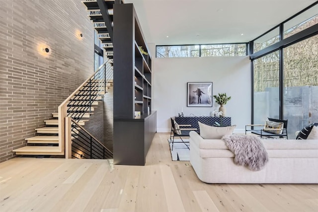 living room with a towering ceiling, light hardwood / wood-style flooring, expansive windows, and brick wall