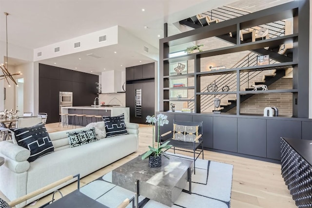 living room with a high ceiling, sink, an inviting chandelier, and light hardwood / wood-style flooring