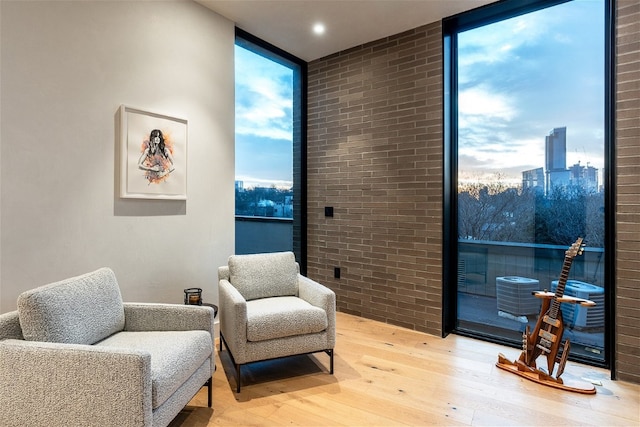 sitting room featuring expansive windows, brick wall, and hardwood / wood-style floors