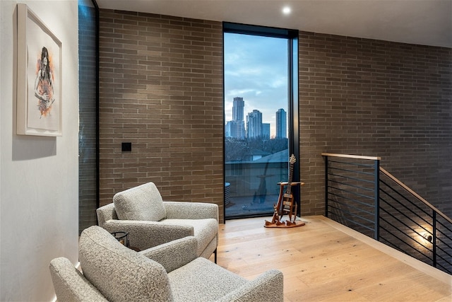 living area with expansive windows, brick wall, and hardwood / wood-style floors