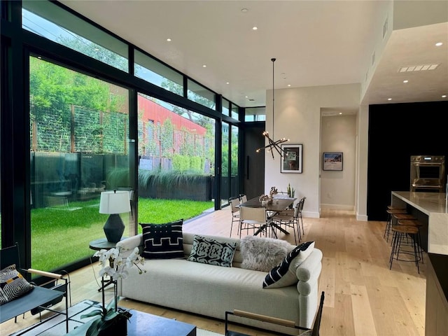 living room with an inviting chandelier, a wall of windows, and light wood-type flooring