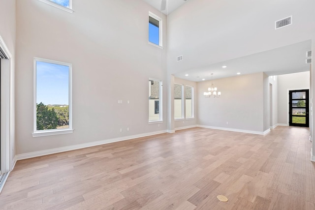 unfurnished living room featuring light wood-type flooring, a towering ceiling, an inviting chandelier, and a wealth of natural light