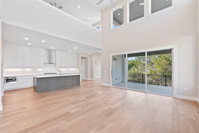 unfurnished living room with ceiling fan, sink, a towering ceiling, and light wood-type flooring