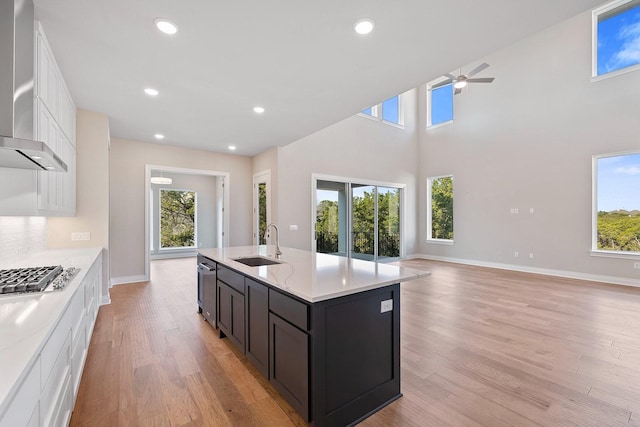 kitchen with sink, wall chimney range hood, a center island with sink, white cabinets, and appliances with stainless steel finishes