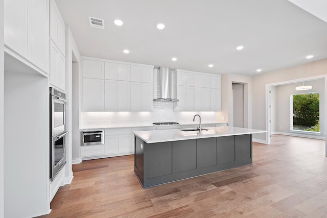 kitchen with white cabinetry, sink, wall chimney range hood, and a center island with sink