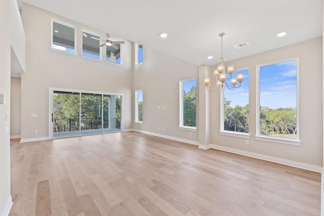 unfurnished living room with a high ceiling, plenty of natural light, light hardwood / wood-style floors, and ceiling fan with notable chandelier