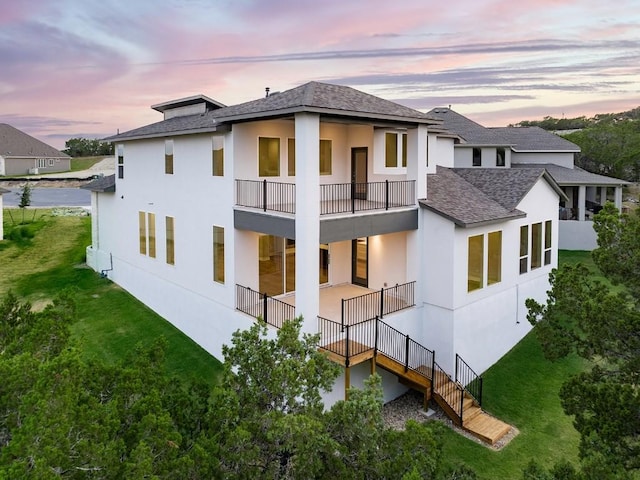 back house at dusk featuring a balcony and a yard