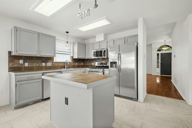 kitchen with appliances with stainless steel finishes, backsplash, sink, pendant lighting, and a center island