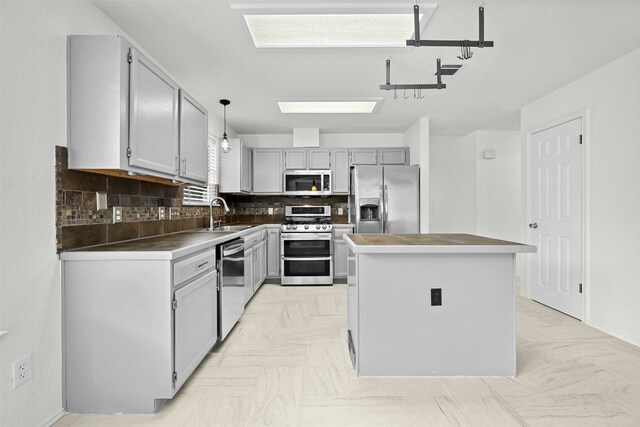 kitchen with a center island, hanging light fixtures, stainless steel appliances, backsplash, and gray cabinets