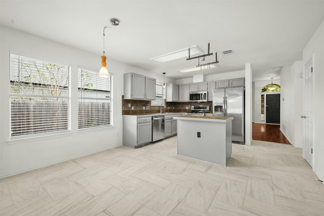 kitchen featuring appliances with stainless steel finishes, backsplash, gray cabinetry, pendant lighting, and a kitchen island