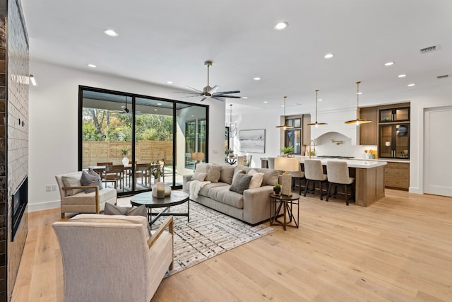 living room with ceiling fan, a large fireplace, and light hardwood / wood-style flooring