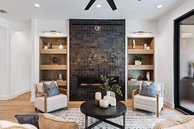 living room with built in shelves, light hardwood / wood-style floors, ceiling fan, and a tiled fireplace