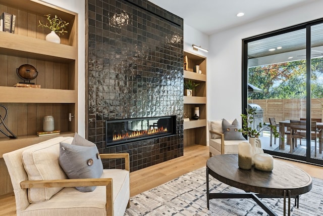 living area with a tile fireplace, built in shelves, and light hardwood / wood-style floors