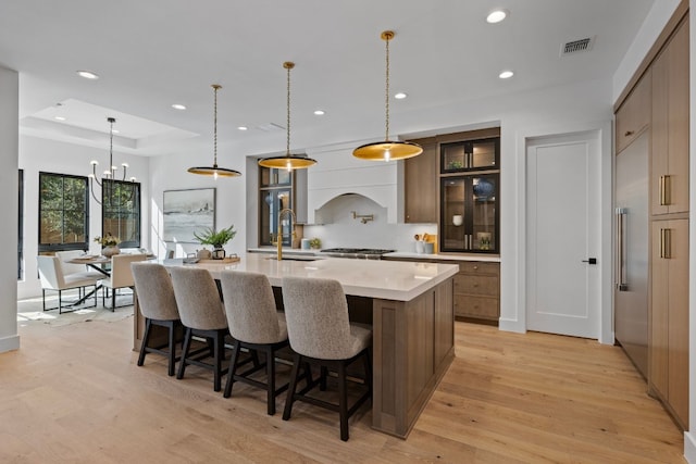 kitchen with a breakfast bar, a large island with sink, sink, hanging light fixtures, and light hardwood / wood-style floors