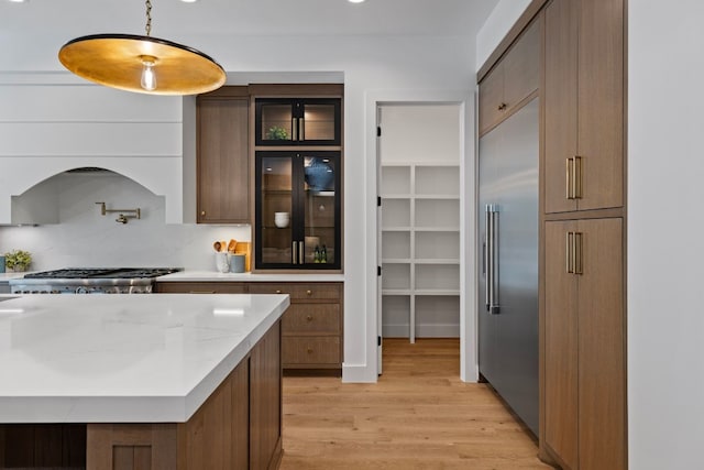 kitchen featuring light stone countertops, light hardwood / wood-style flooring, decorative light fixtures, decorative backsplash, and appliances with stainless steel finishes