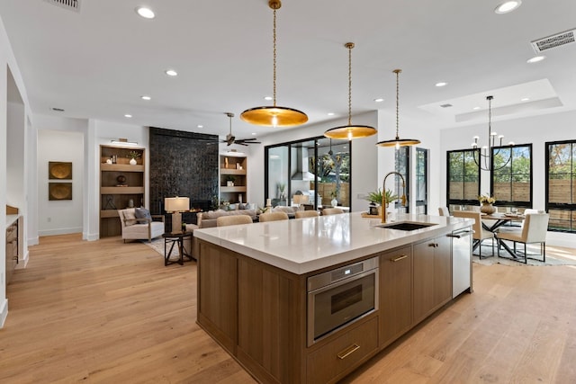 kitchen with ceiling fan with notable chandelier, sink, light hardwood / wood-style floors, hanging light fixtures, and an island with sink