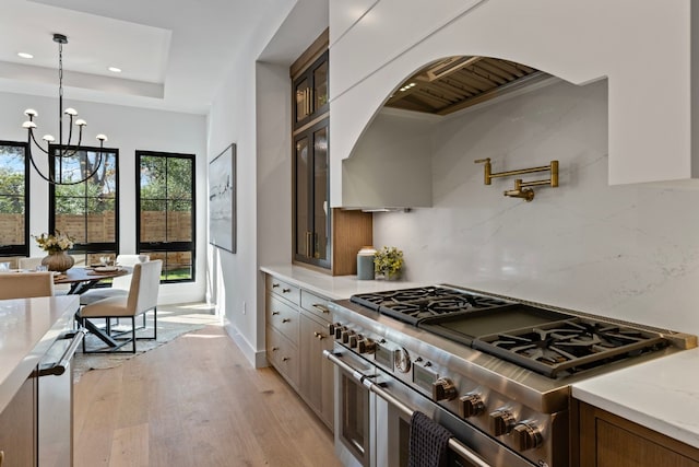 kitchen featuring double oven range, a raised ceiling, light stone countertops, light hardwood / wood-style floors, and a chandelier