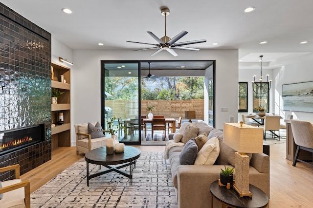 living room with a fireplace, light wood-type flooring, and ceiling fan with notable chandelier