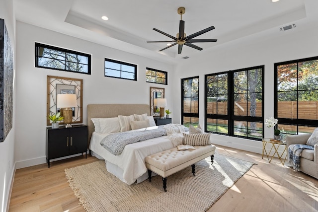 bedroom with a raised ceiling, multiple windows, ceiling fan, and light hardwood / wood-style floors