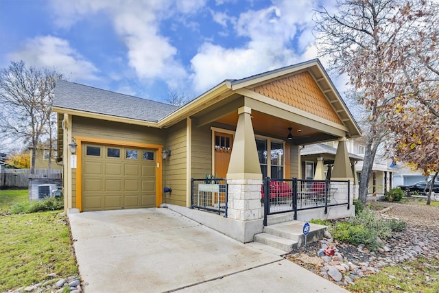 craftsman house with a shingled roof, concrete driveway, an attached garage, a porch, and central AC