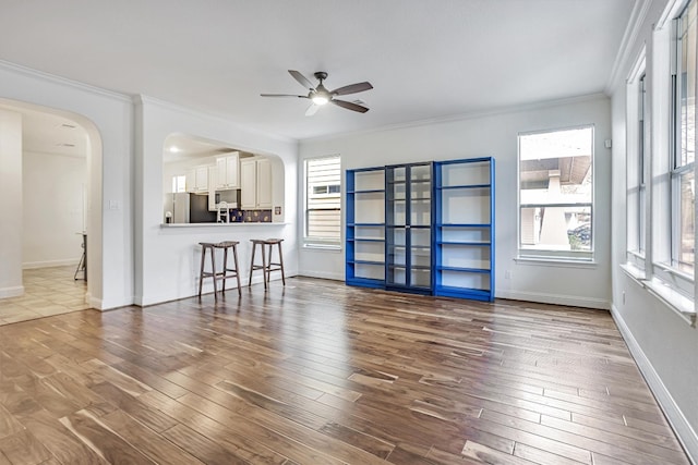 living room featuring arched walkways, ceiling fan, wood finished floors, baseboards, and crown molding