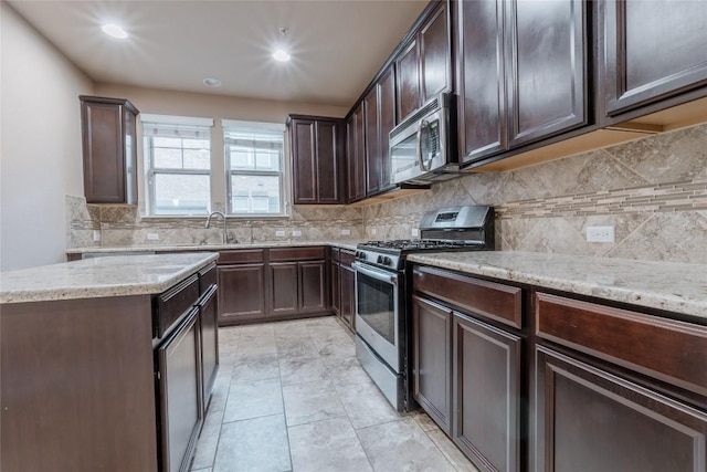 kitchen featuring sink, light stone countertops, appliances with stainless steel finishes, tasteful backsplash, and dark brown cabinets