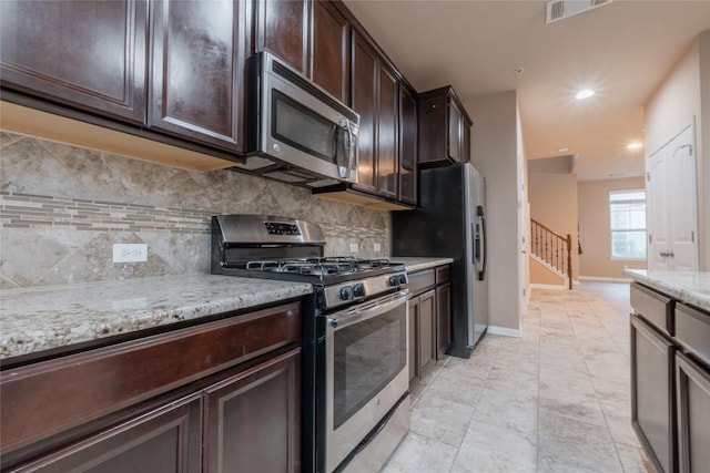 kitchen with dark brown cabinetry, light stone countertops, appliances with stainless steel finishes, and tasteful backsplash