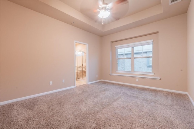 empty room featuring a raised ceiling, ceiling fan, and carpet floors