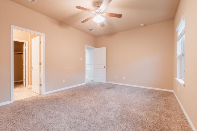 unfurnished bedroom with a walk in closet, light colored carpet, and ceiling fan