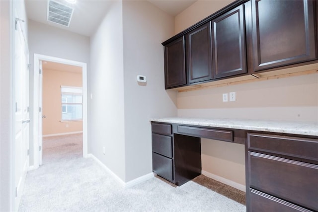 interior space with dark brown cabinets, built in desk, and light carpet