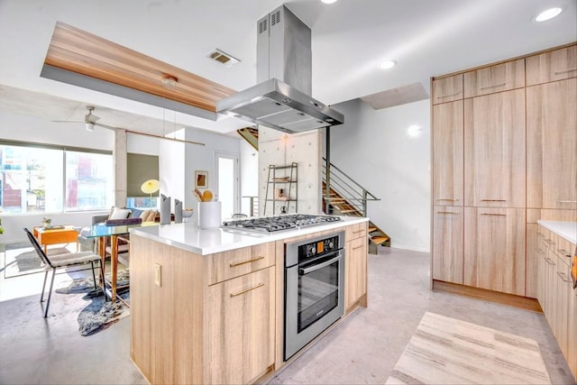 kitchen with ceiling fan, appliances with stainless steel finishes, a center island, island range hood, and light brown cabinets