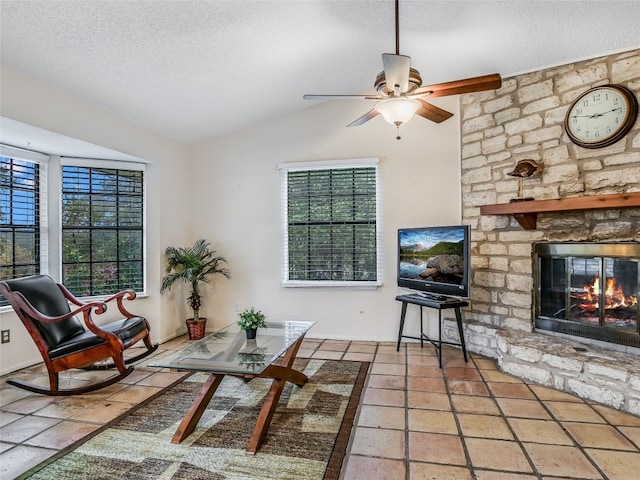 living room with ceiling fan, a stone fireplace, a textured ceiling, and vaulted ceiling