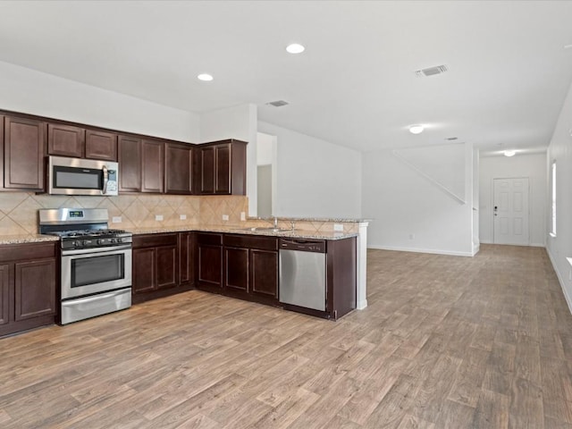 kitchen with sink, tasteful backsplash, light hardwood / wood-style floors, light stone counters, and stainless steel appliances