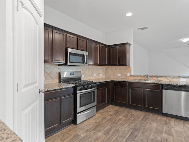 kitchen featuring stainless steel appliances, light stone counters, hardwood / wood-style flooring, and sink