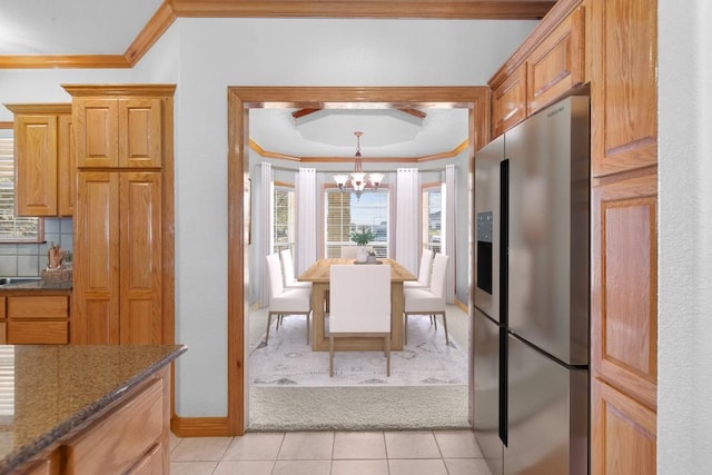 kitchen with dark stone counters, crown molding, stainless steel refrigerator with ice dispenser, light tile patterned floors, and a chandelier