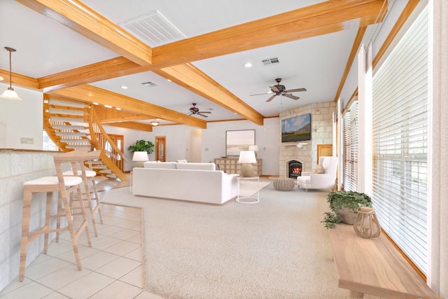 living room with ceiling fan, a fireplace, beamed ceiling, and light tile patterned floors