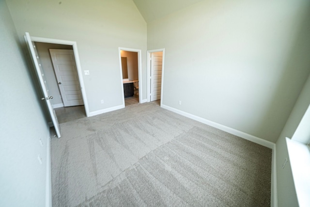 unfurnished bedroom with a walk in closet, ensuite bathroom, high vaulted ceiling, and light colored carpet