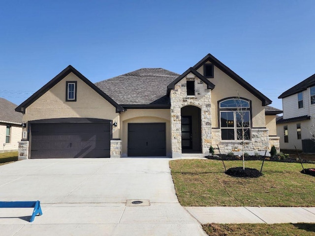 french country style house with an attached garage, stone siding, driveway, and stucco siding